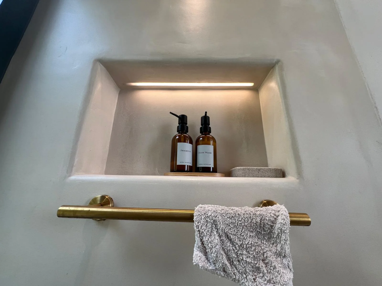 Nicho integrado con microcemento, LED y toallero bronce — baño Ibiza